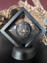 Photo of a black plastic display case with clear film in the centre. The case is a square, sitting on a corner (like a diamond). The bottom is fitted into a black base so it stands upright. The case is holding a sobriety chip showing 666 Days.
A piece of driftwood is in the background.