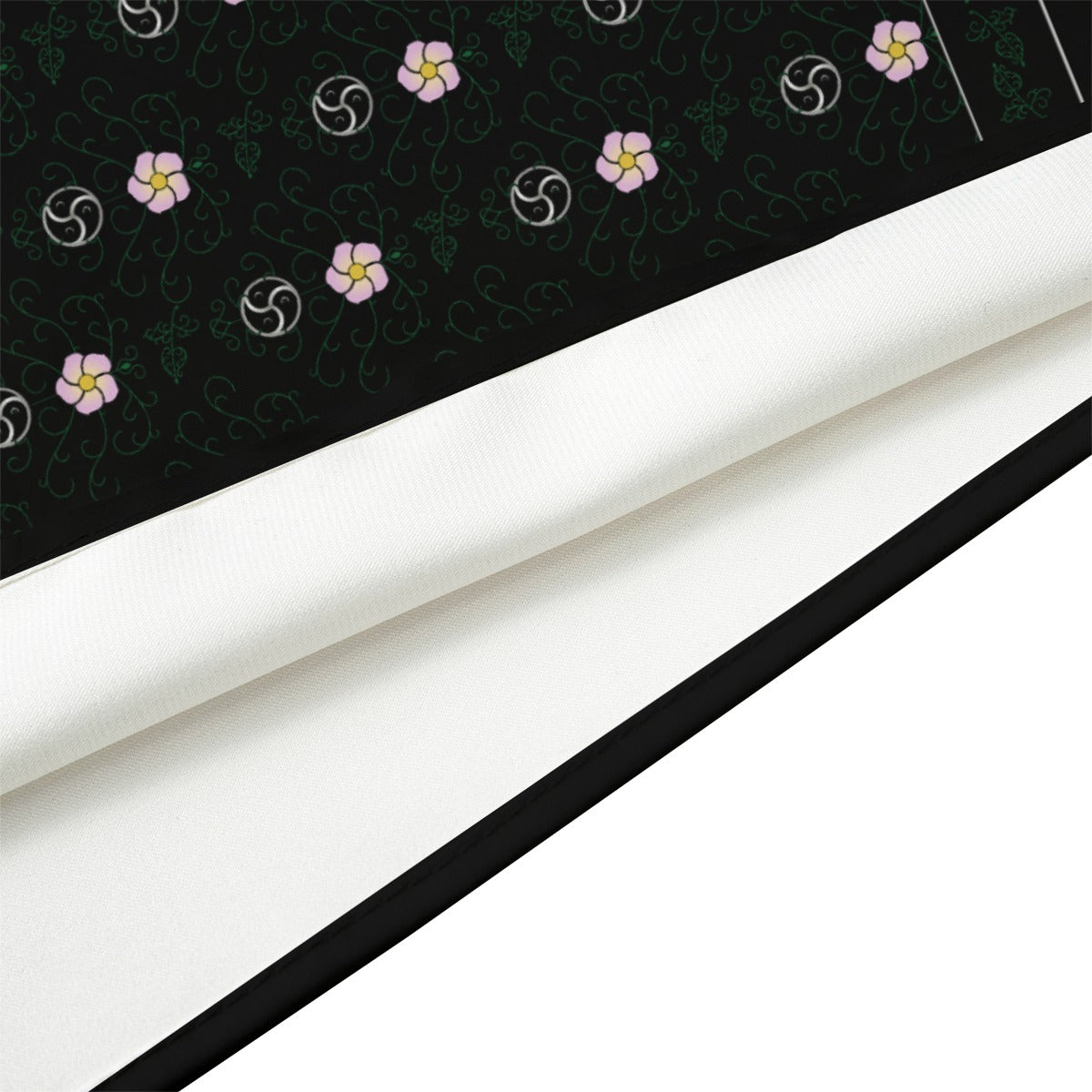 A close-up, angled macro shot of the 'Kinky' (black) silk bandana, showing the fabric detail, black stitched hem, and the white reverse side.