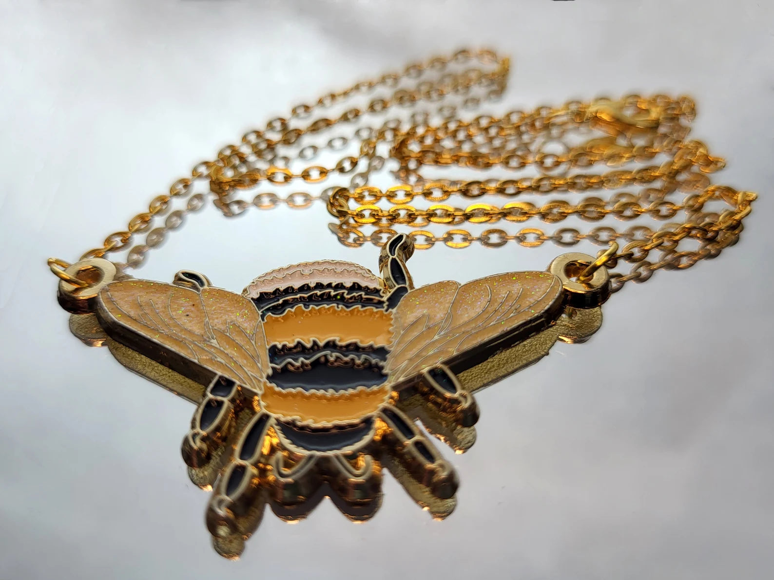 Photo of a white-tailed bumblebee enamel pendant with gold chain, resting on a mirror.